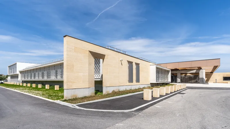 Corner view of the beige masonry facade with patterned screen panels and planted gravel beds