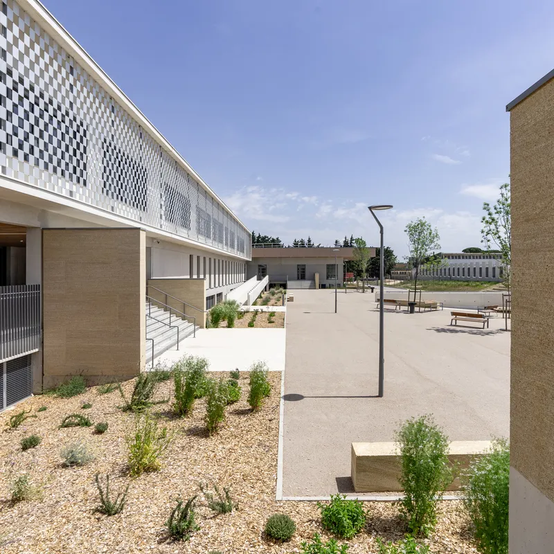 Courtyard with gravel-mulched planting beds between concrete paved areas and perforated facade screen