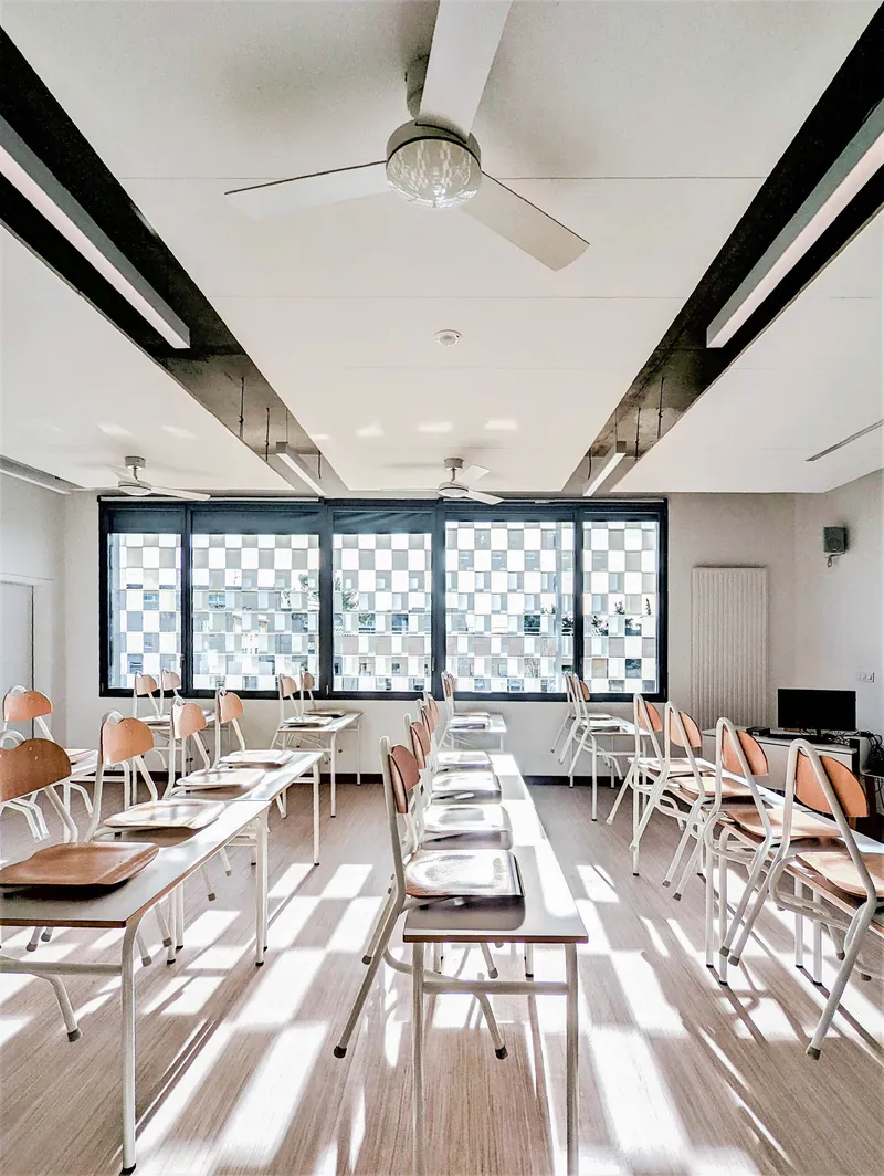 Dining hall with white metal chairs and checkered glass windows filtering daylight across the pale timber floor