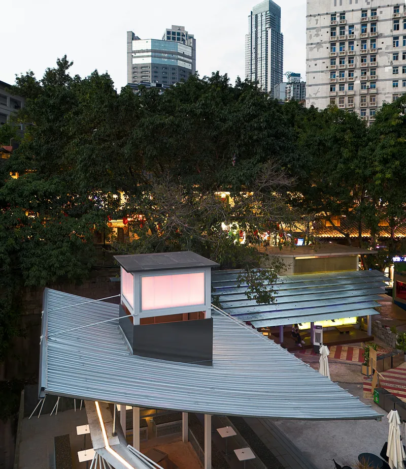 Aerial view of curved corrugated metal roofs sheltering a courtyard surrounded by mature trees at twilight