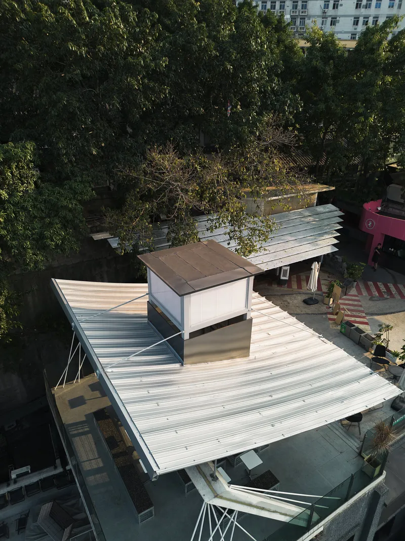 Overhead view of ribbed metal roof planes wrapping around a central skylit volume in morning light