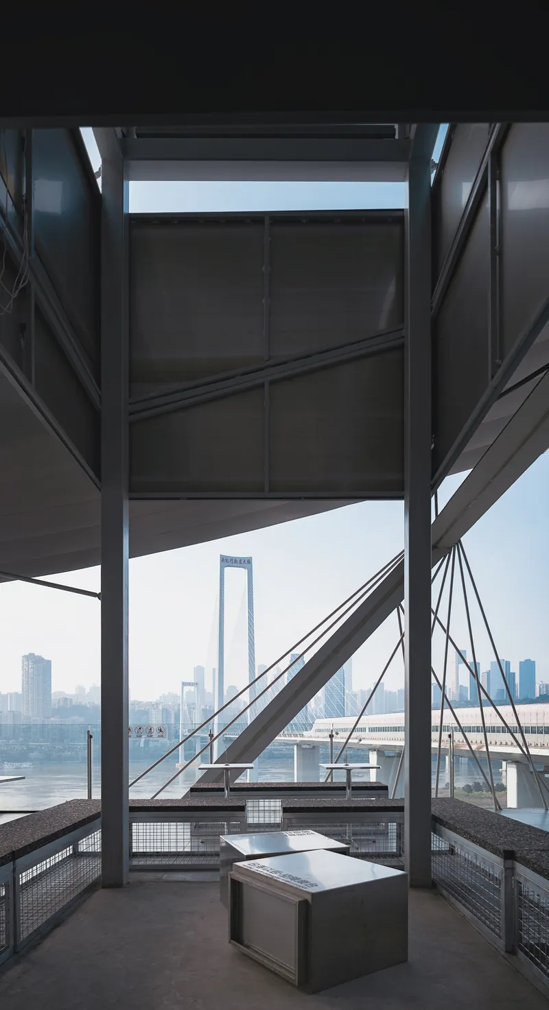View through steel structural bracing toward a waterfront bridge under a misty sky