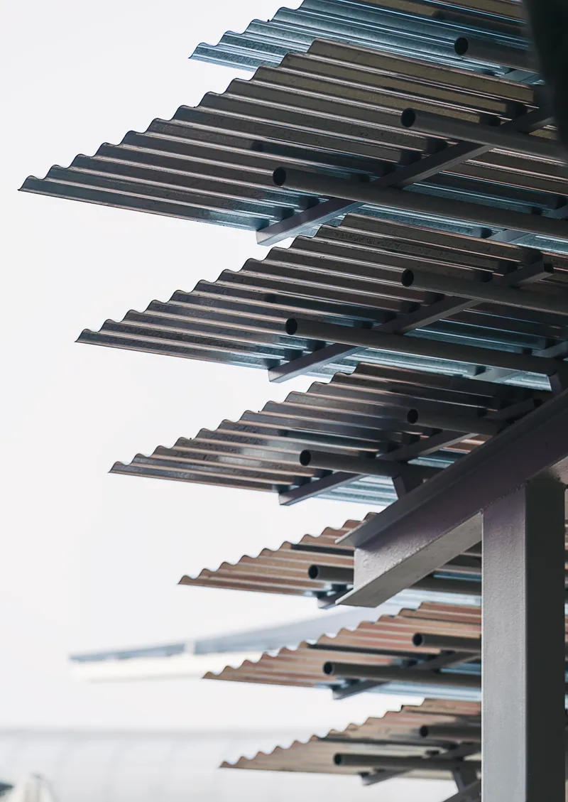 Upward view of cantilevered metal louvres extending from a white facade against an overcast sky