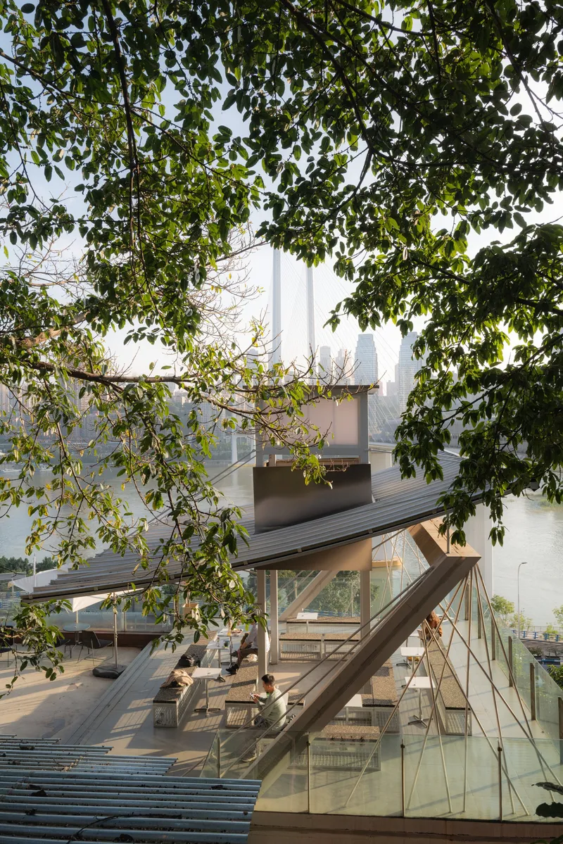View through tree branches of an open timber pavilion with glass balustrade in morning haze