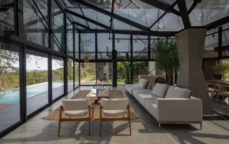 Glass-walled living room with exposed steel trusses overhead and a pool terrace visible beyond