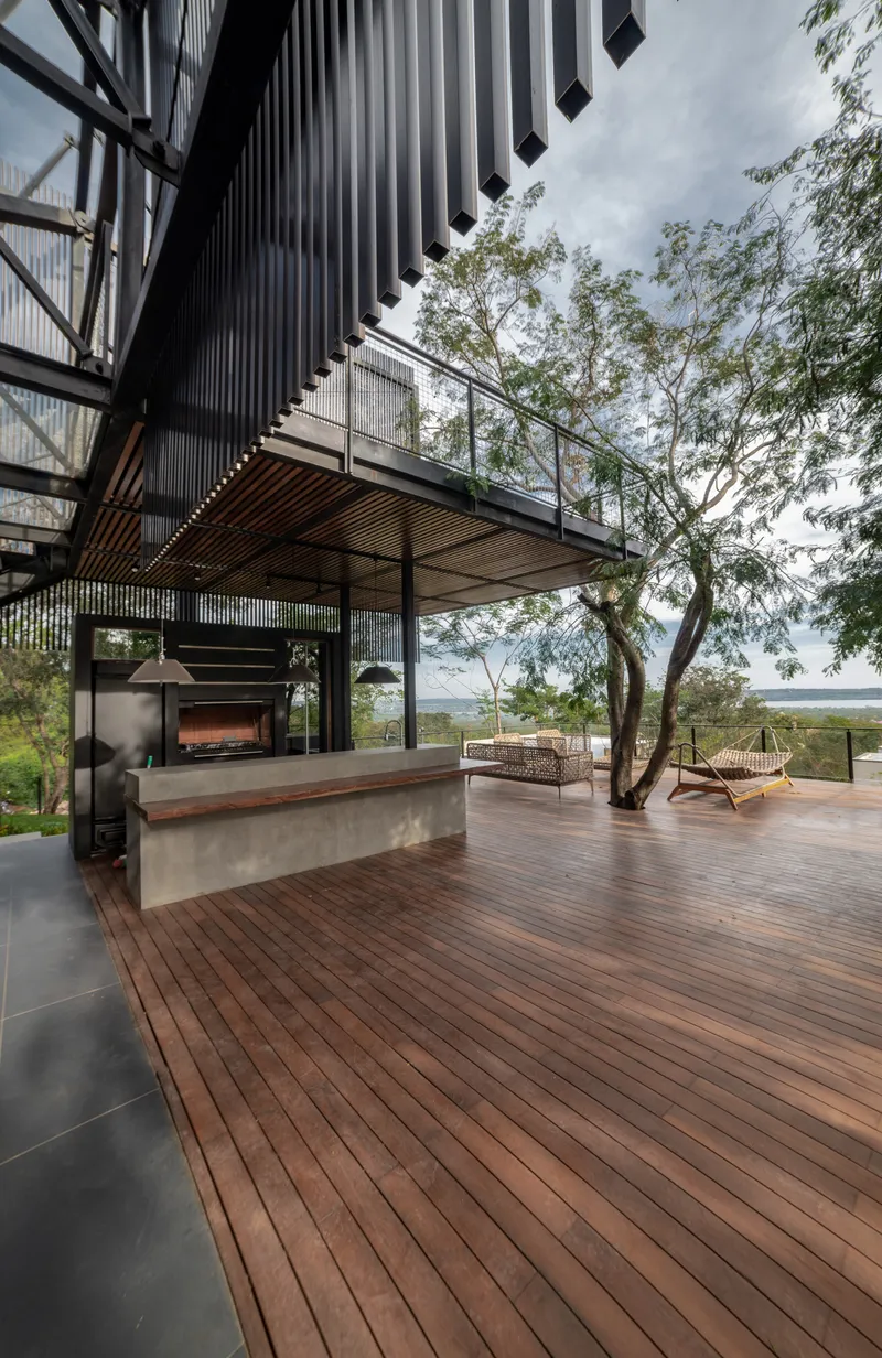 Timber deck with concrete fireplace under a corrugated metal canopy and tree growing through