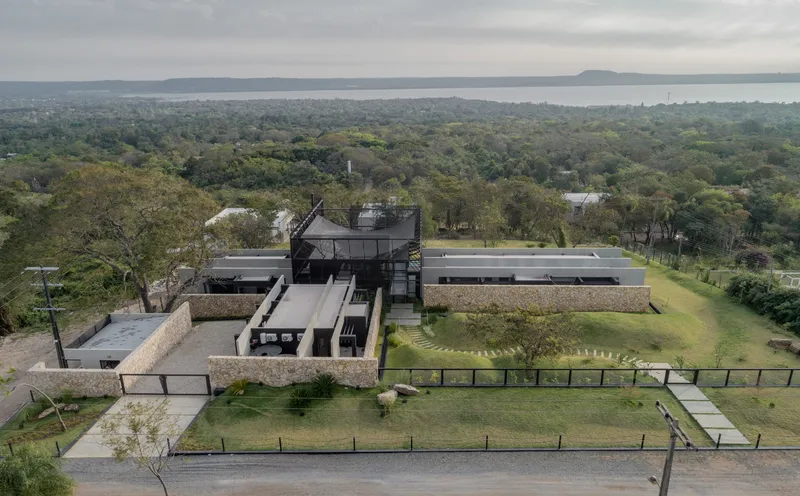Aerial view of the stone-clad and dark metal volumes arranged around landscaped courtyards with a lake beyond