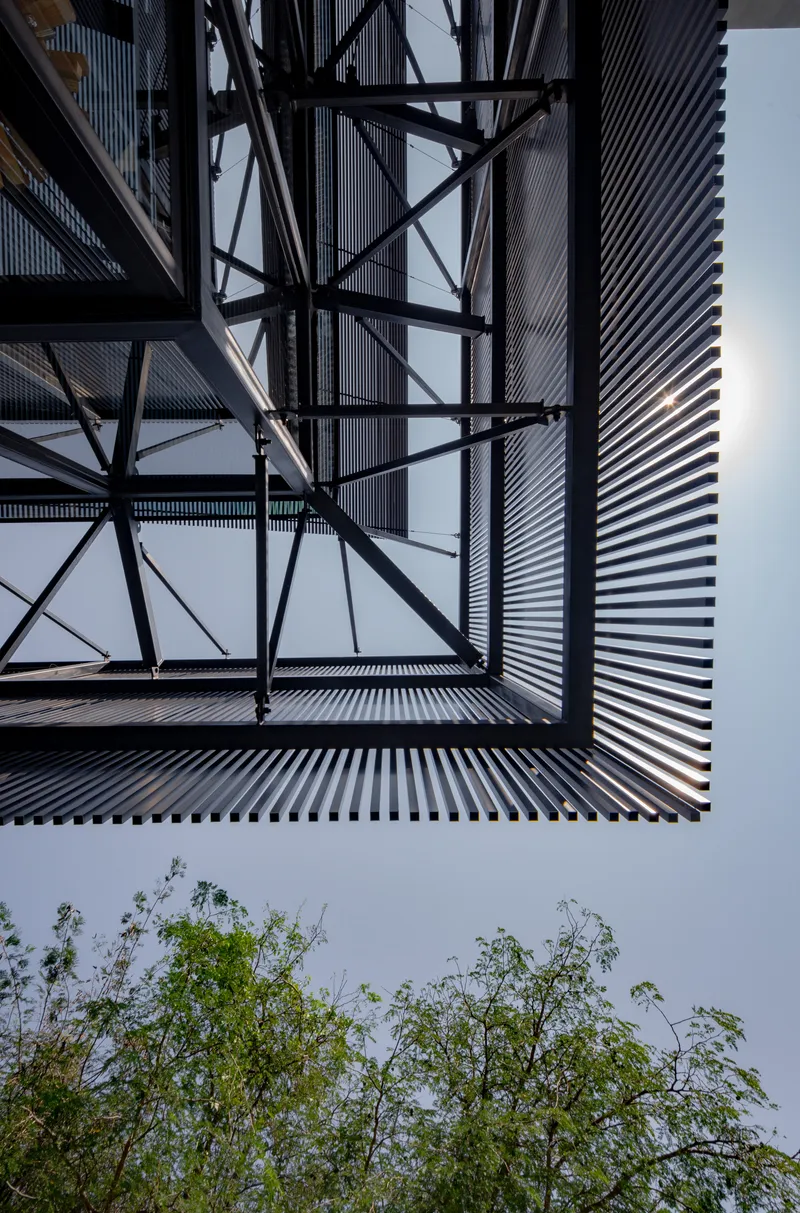 Upward view of the diagonal steel bracing and corrugated facade with treetops visible below
