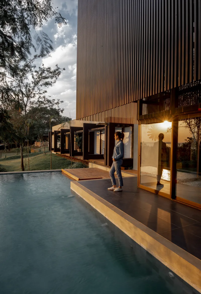 Two figures on the poolside deck at dusk beneath the vertical louvered facade and cloudy sky