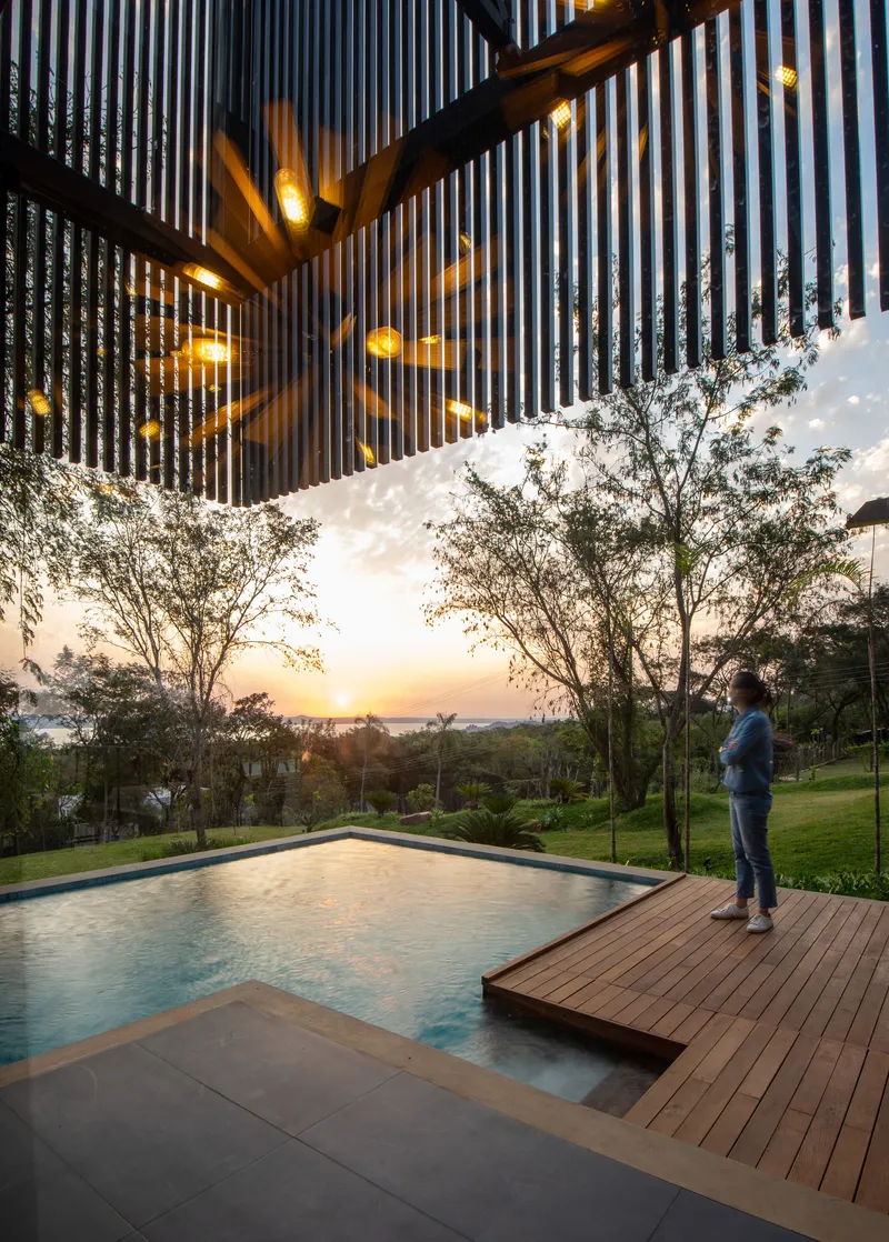 Figure standing on timber deck beside the pool at sunset with pendant lights overhead