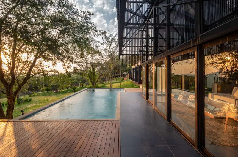 Timber deck terrace with lap pool alongside floor-to-ceiling glazing at golden hour