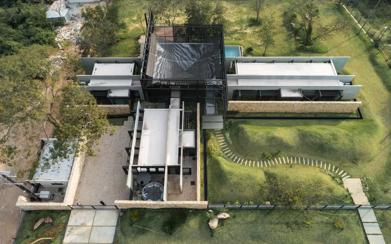 Overhead drone photograph of the cross-shaped residence with white roof planes and central steel tower