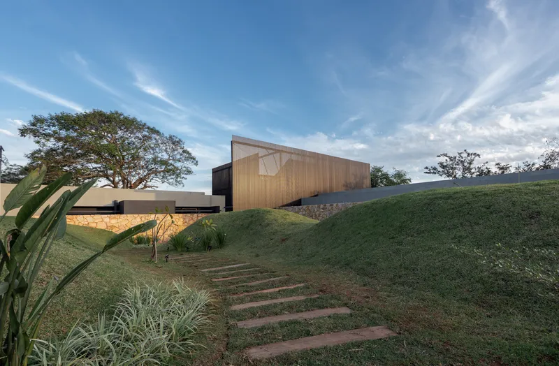 Timber-clad upper volume hovering above stone base wall with stepping stones ascending the slope