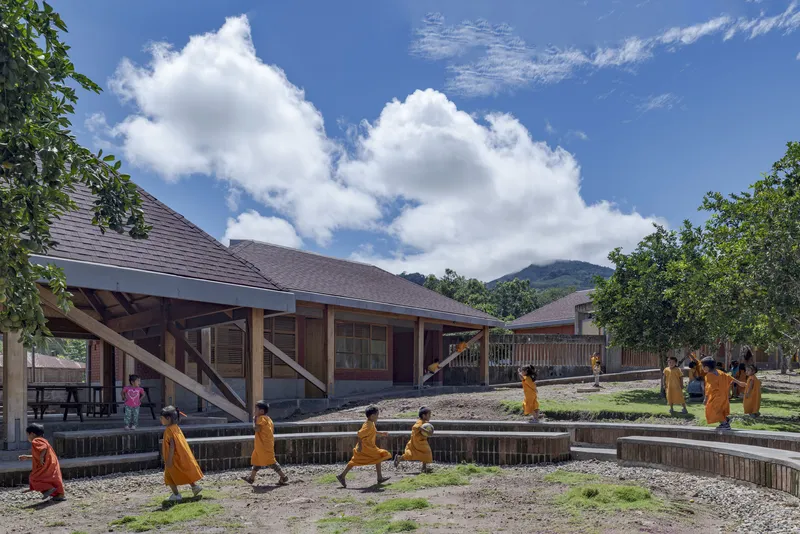 Courtyard with low-slung pitched roof buildings and stepped timber retaining walls as children walk along the pathways