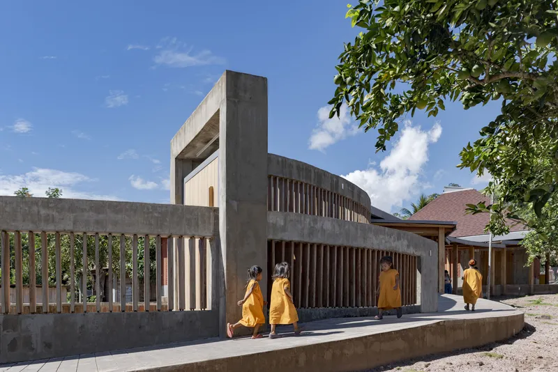 Curved concrete wall with vertical slatted screening leading to a tower-like portal as figures walk the pathway
