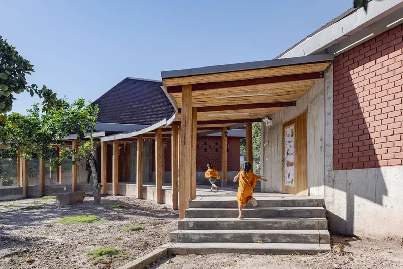 Timber-framed entry portico with exposed rafters and concrete steps leading to red brick walls beyond