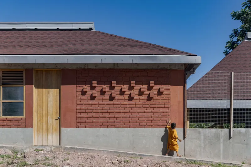 Red brick facade with protruding brick patterns and timber door set above a smooth concrete base wall