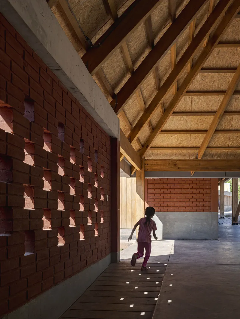 Perforated brick wall casting patterned shadows on the floor as a child runs through the corridor