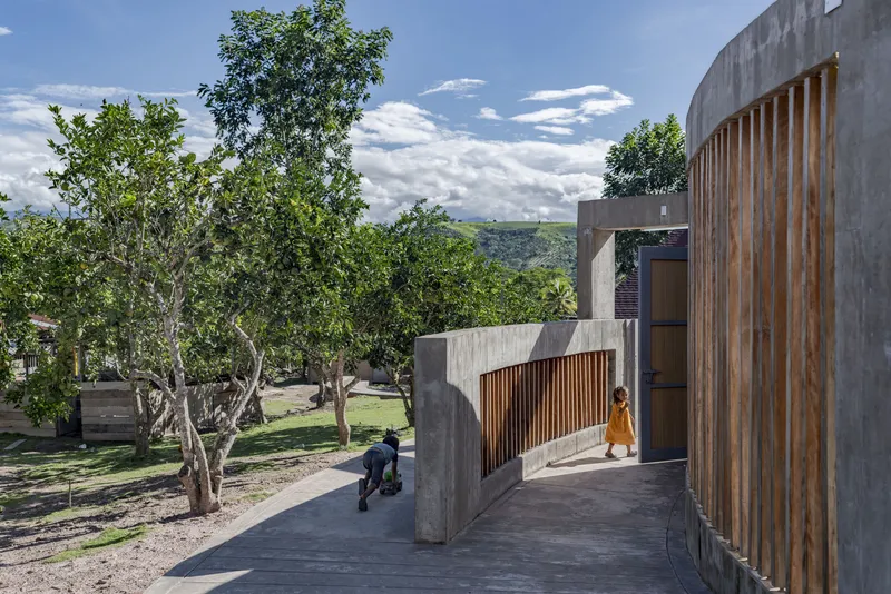 Elevated concrete walkway with vertical timber screens, children walking beside trees under a cloudy sky