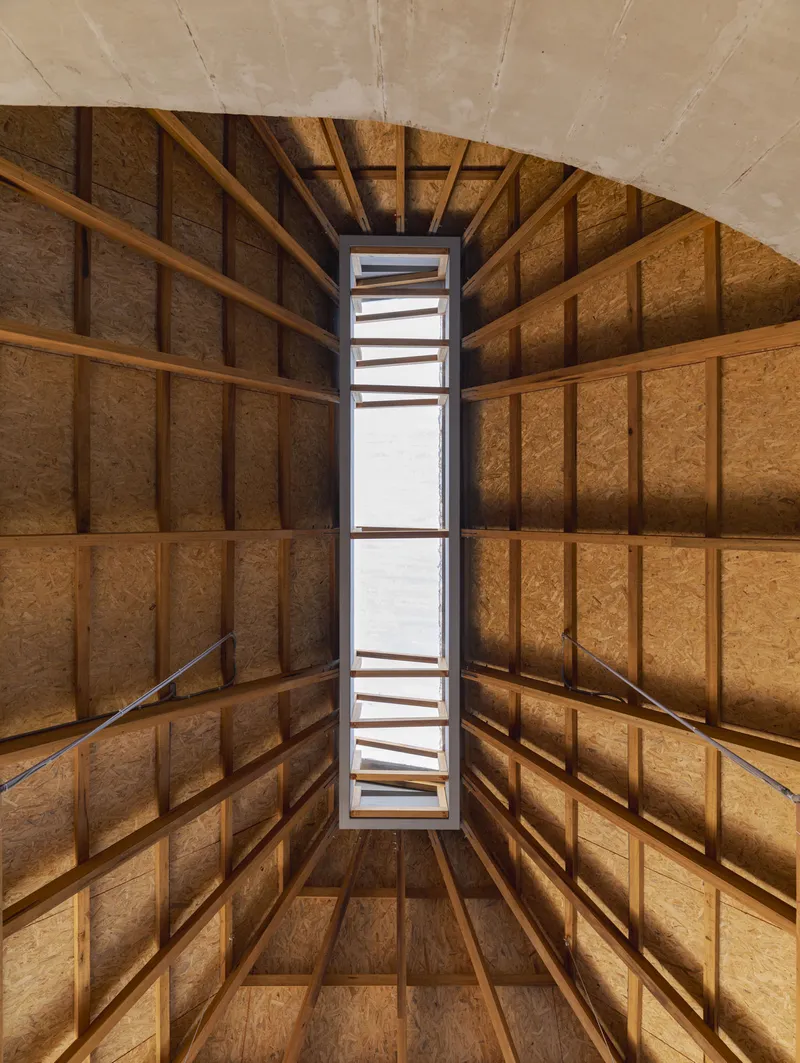 Upward view of a vertical skylight framed by exposed timber beams and oriented strand board panels