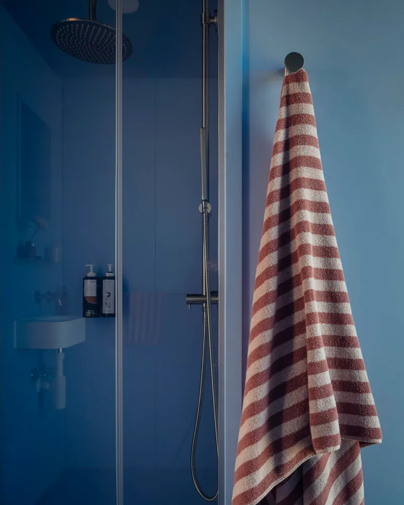 Glass shower enclosure with overhead rain head and striped towel hanging on blue wall