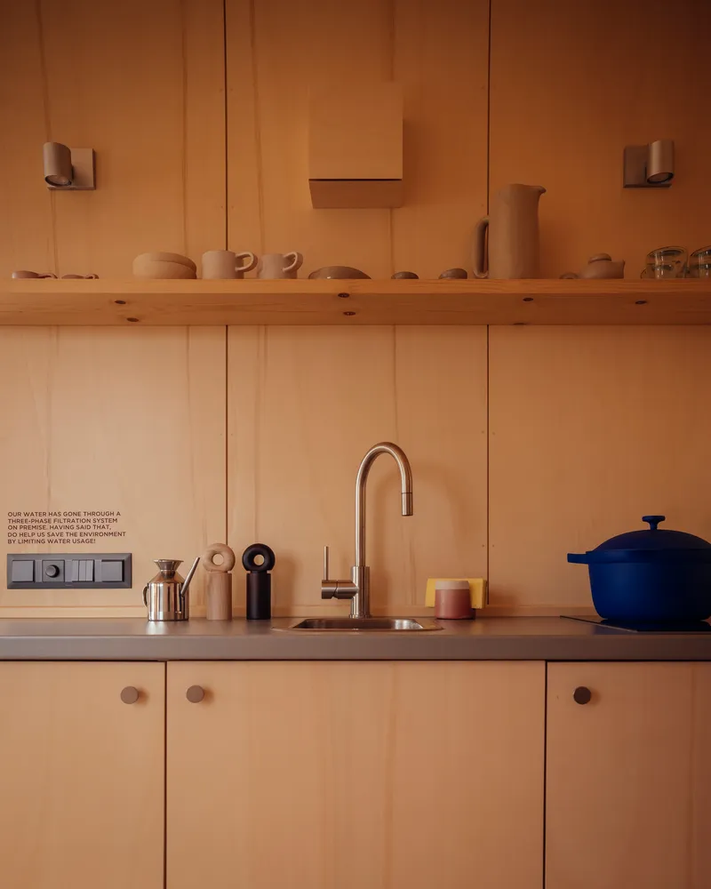 Kitchen counter with timber paneling, open shelf displaying ceramics, and gooseneck faucet at sink