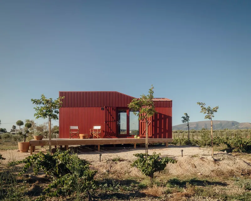 Red corrugated metal pavilion with covered deck and planted terrace in a dry landscape