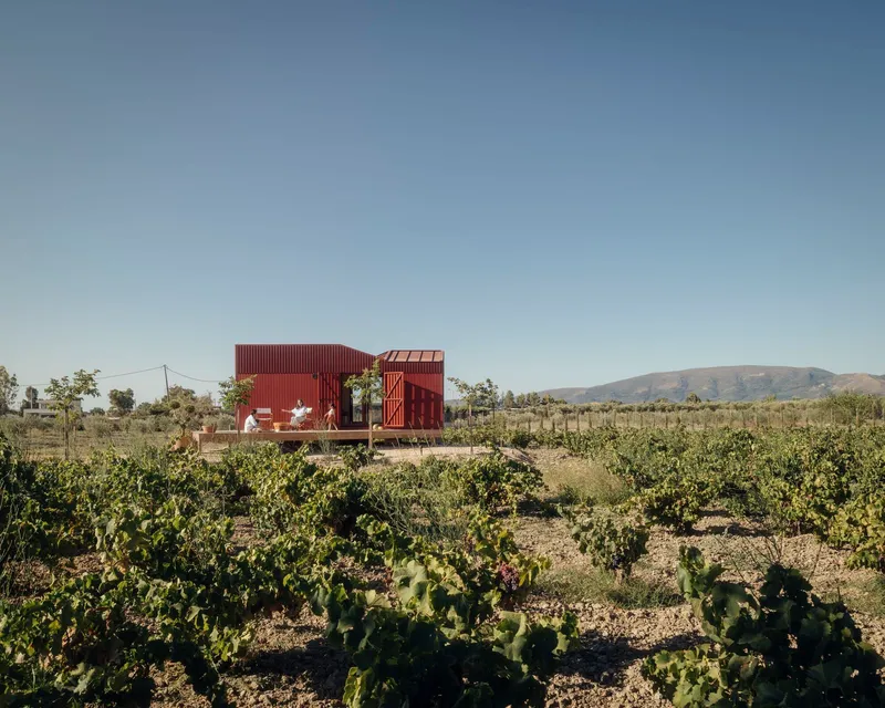 Red corrugated metal volumes set on a raised platform amid a vineyard with distant hills