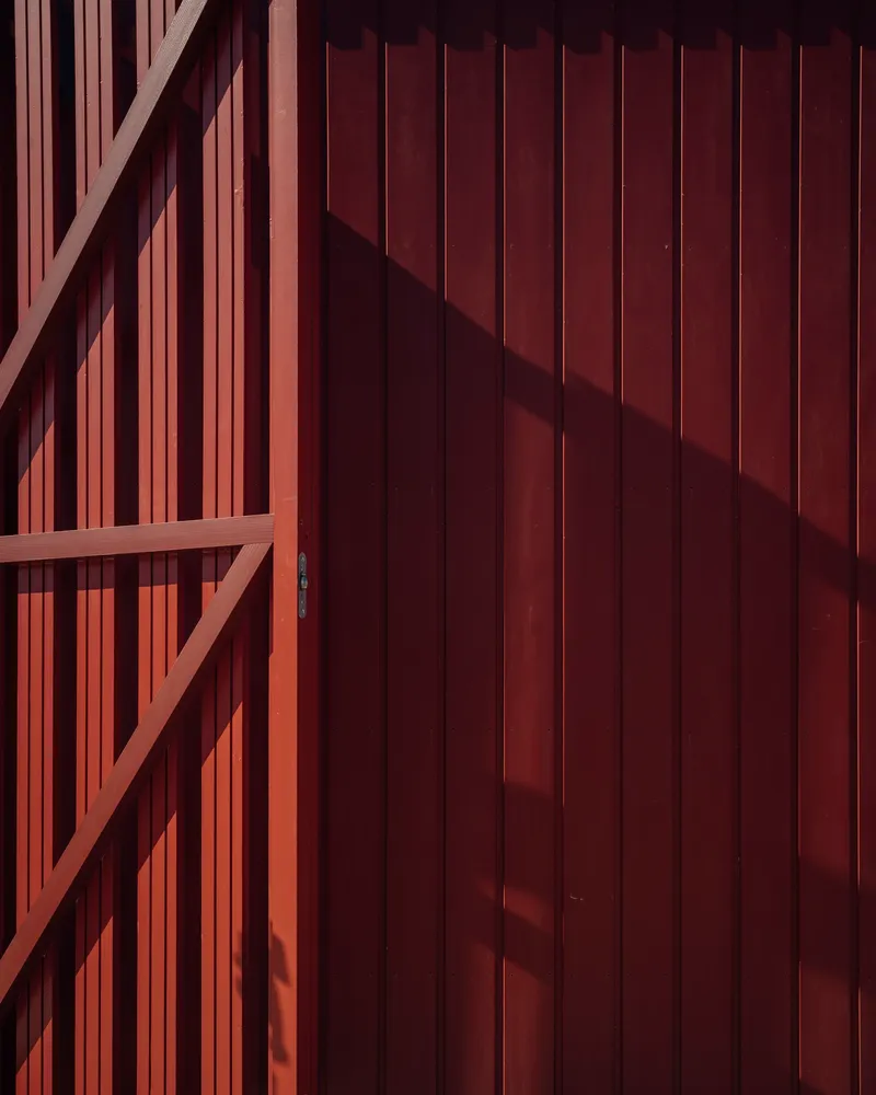 Timber-framed sliding door with vertical battens casting angular shadows across the red-stained wood cladding