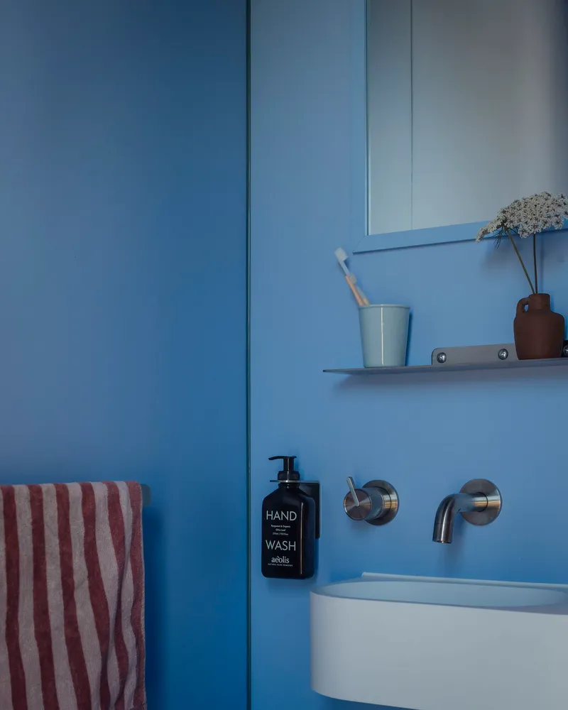Wall-mounted basin with circular chrome taps and shelf against powder blue tiled surfaces