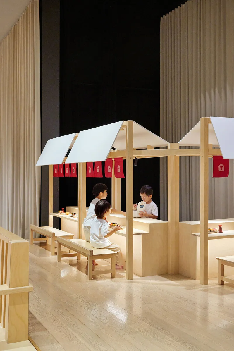 Timber playhouse with white fabric roof and red curtain panels as children sit inside