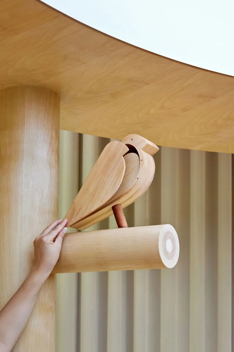 Hand reaching for a wooden bird sculpture mounted on a cylindrical peg beside fabric curtains