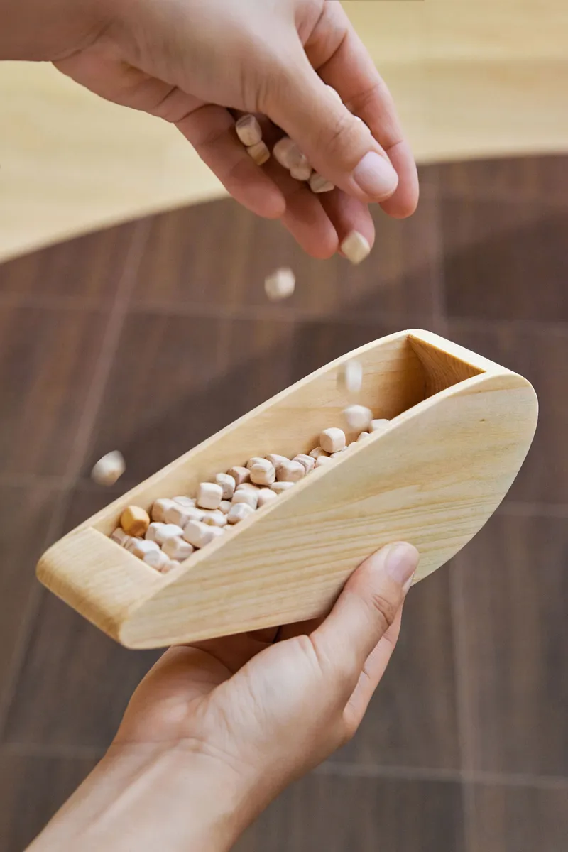 Hand dropping wooden beads into a boat-shaped toy held above dark wood floor