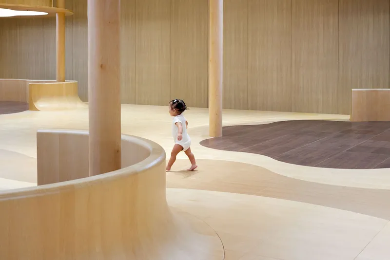 Light wood interior with curved platforms and vertical paneling as a child walks through the space