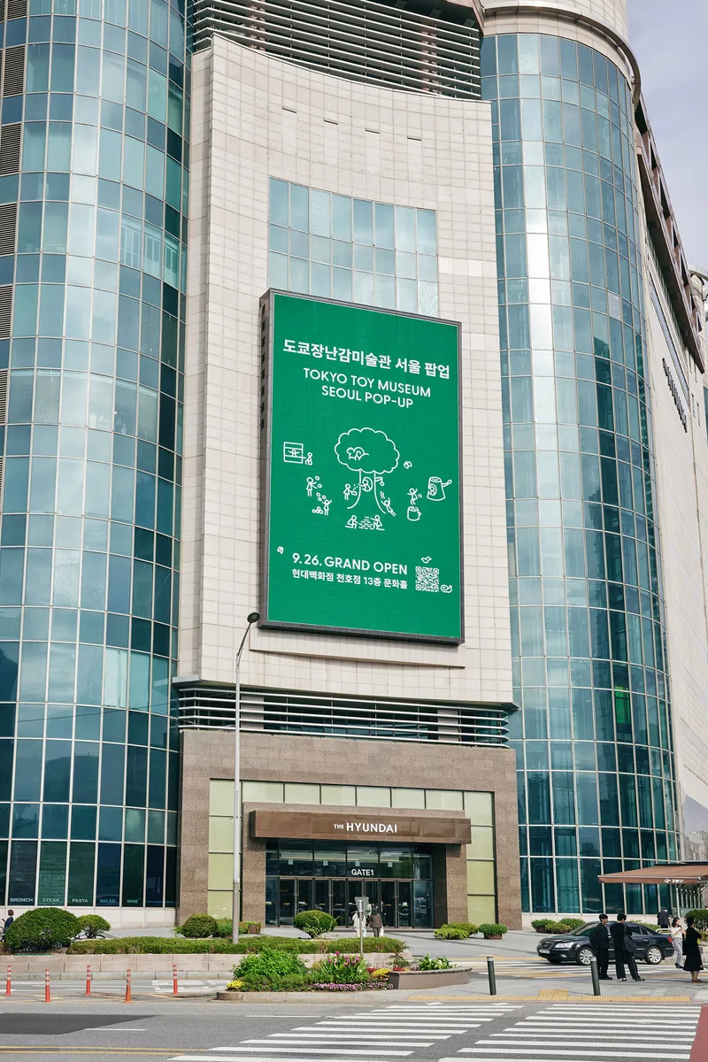 Curved glass and tile facade with large green signage banner above the ground-level entrance