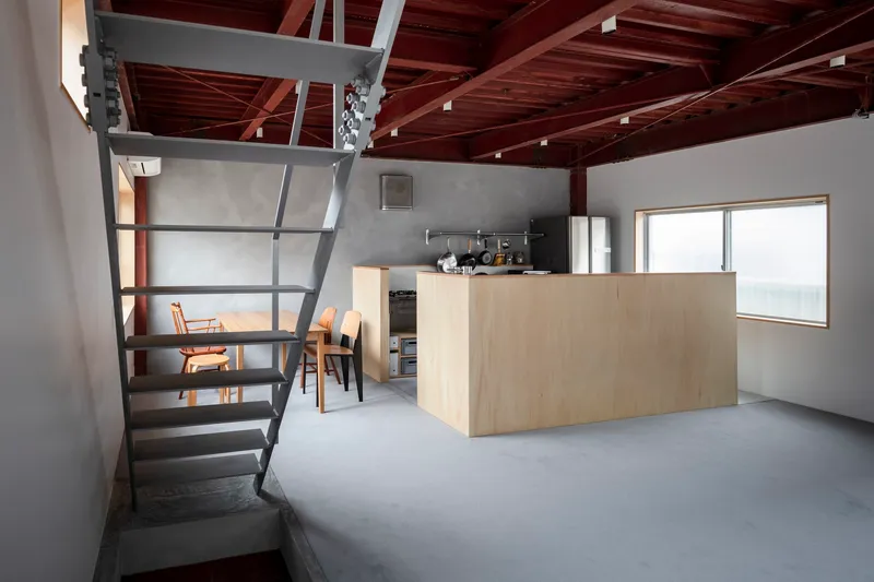 Steel staircase ascending to a loft beside a plywood kitchen island under timber rafters