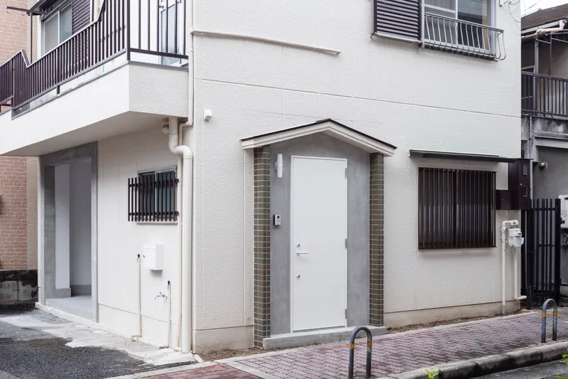 Street view of a white stucco facade with gabled entry and corrugated metal screens