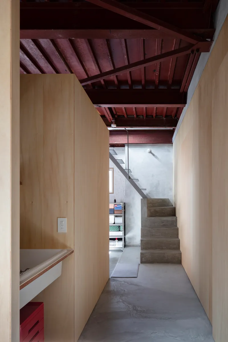 Corridor view toward concrete stairs between plywood walls under an exposed timber structure
