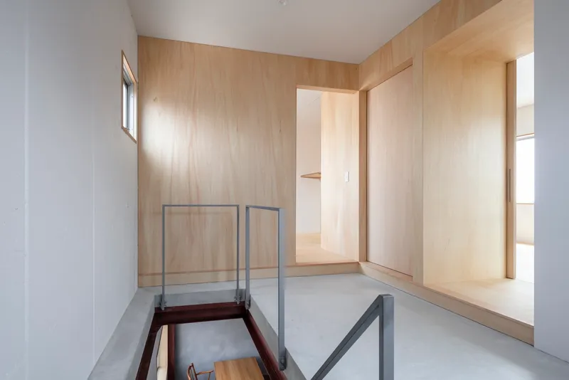 Upper hallway with pale plywood walls and glass-railed opening overlooking the space below