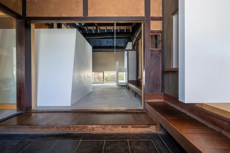 View from raised timber floor across dark stone entry threshold to polished concrete room beyond
