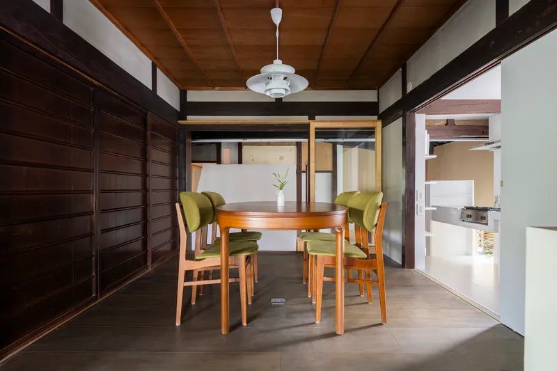 Dining area with timber table, green upholstered chairs and dark wood sliding wall panels under pendant light