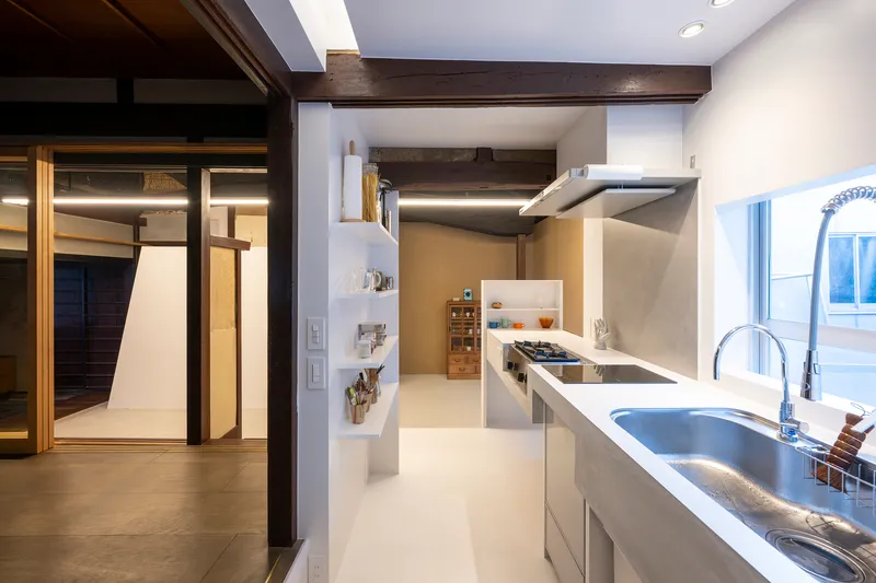 Kitchen interior with white countertops, exposed timber beams and open doorway framing adjacent illuminated corridor