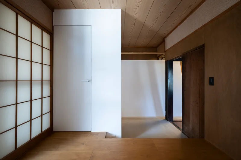 Timber-floored room with translucent shoji screen wall and white partition volume defining an interior threshold