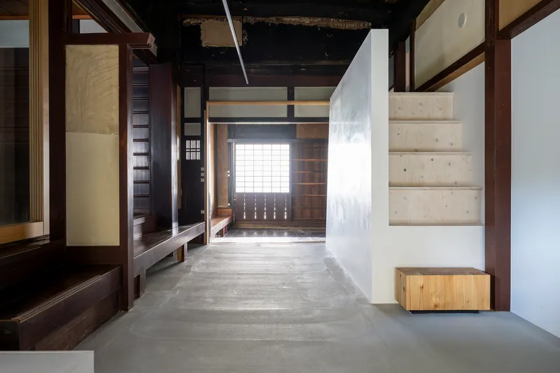Concrete floor hallway with exposed timber structure and white plastered volumes under a dark ceiling