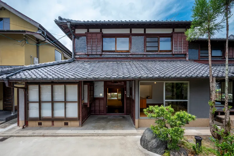 Street facade showing traditional tiled roof above timber framed windows and sliding screens with planted courtyard