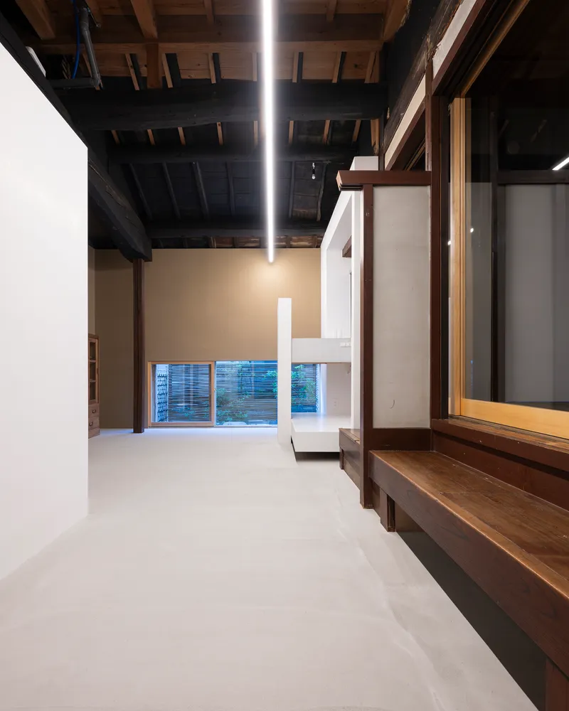 Double-height space with white mezzanine platform inserted beneath blackened timber roof structure and linear lighting