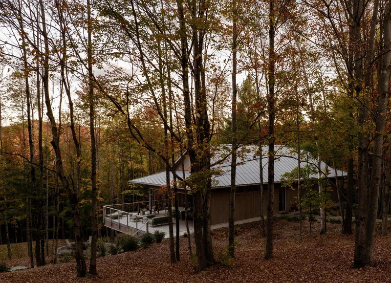 Side view of the cantilevered deck and metal roof through bare autumn trees