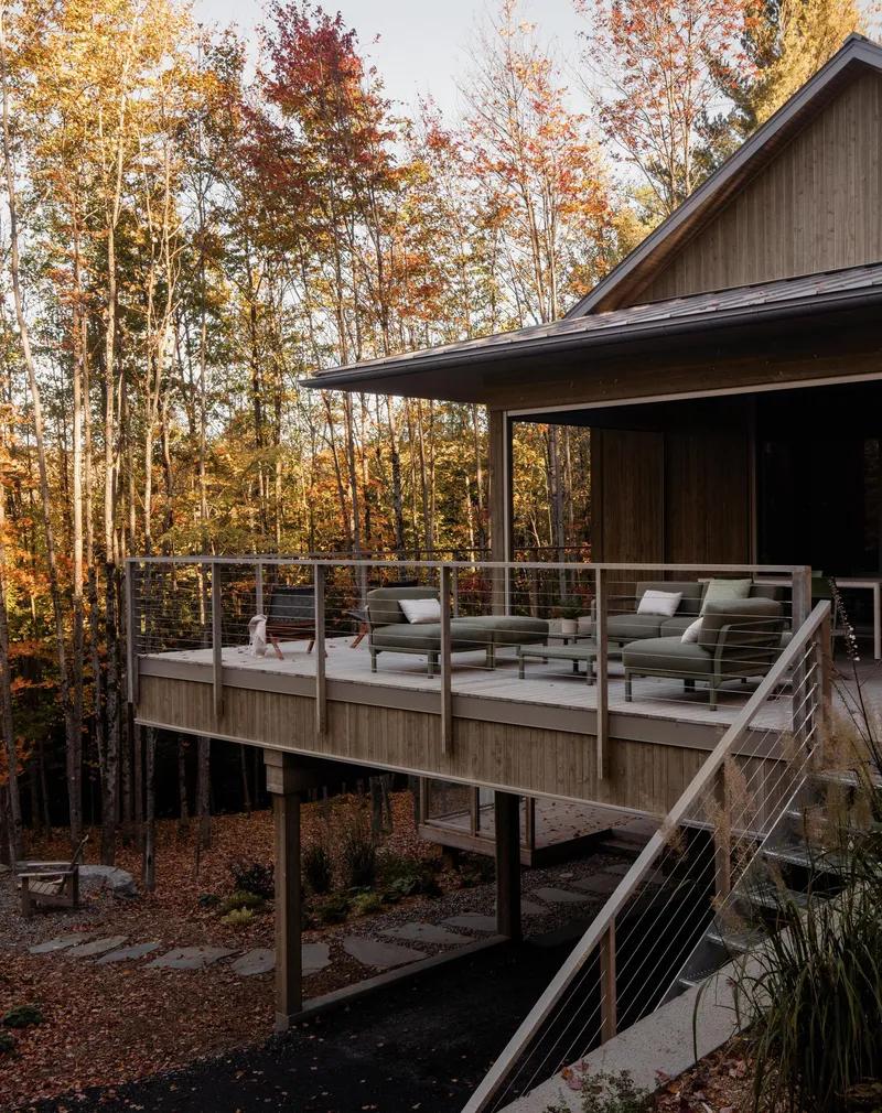 Elevated deck with cable railing and outdoor seating among autumn trees