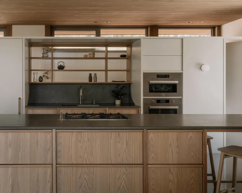 Kitchen with oak-grain cabinetry, dark stone counters and timber-framed open shelving beneath a slatted wood ceiling