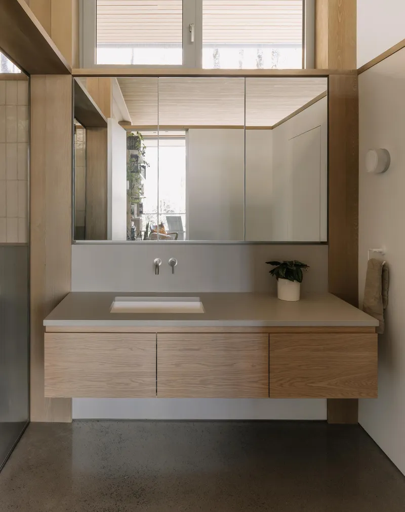 Floating vanity with timber base and mirrored medicine cabinet reflecting a window and potted plant beyond